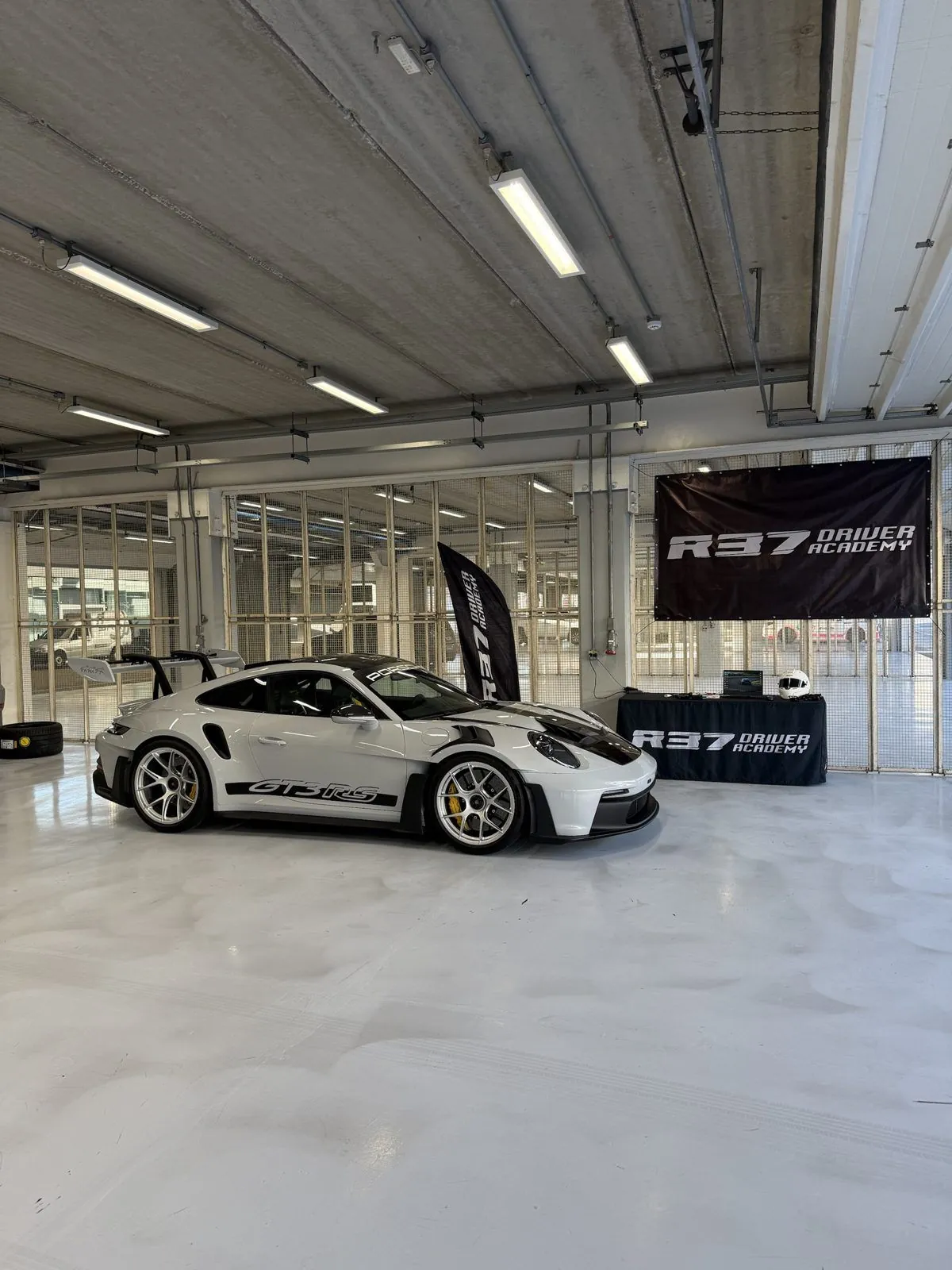 Porsche 911 GT3 RS no box da R37 Driver Academy, com banners da marca e a mesa de análise de dados