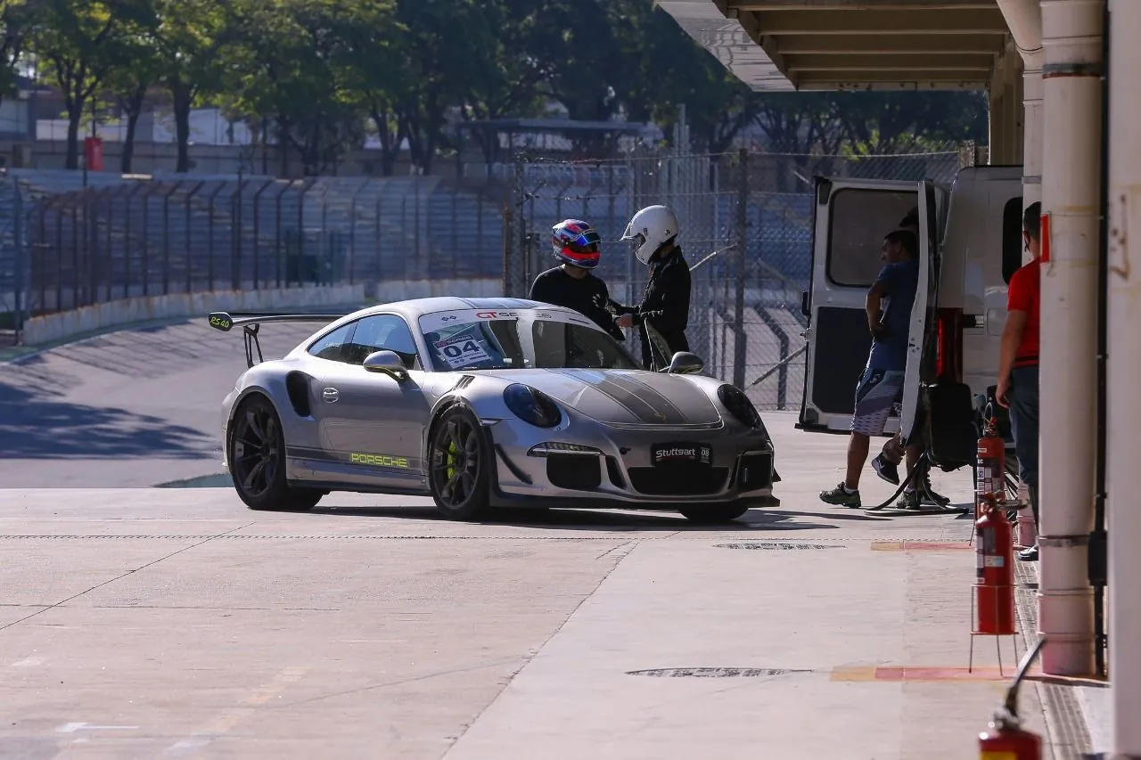 Instrutor e aluno de capacete conversando ao lado de um Porsche 911 GT3 RS nos boxes de Interlagos