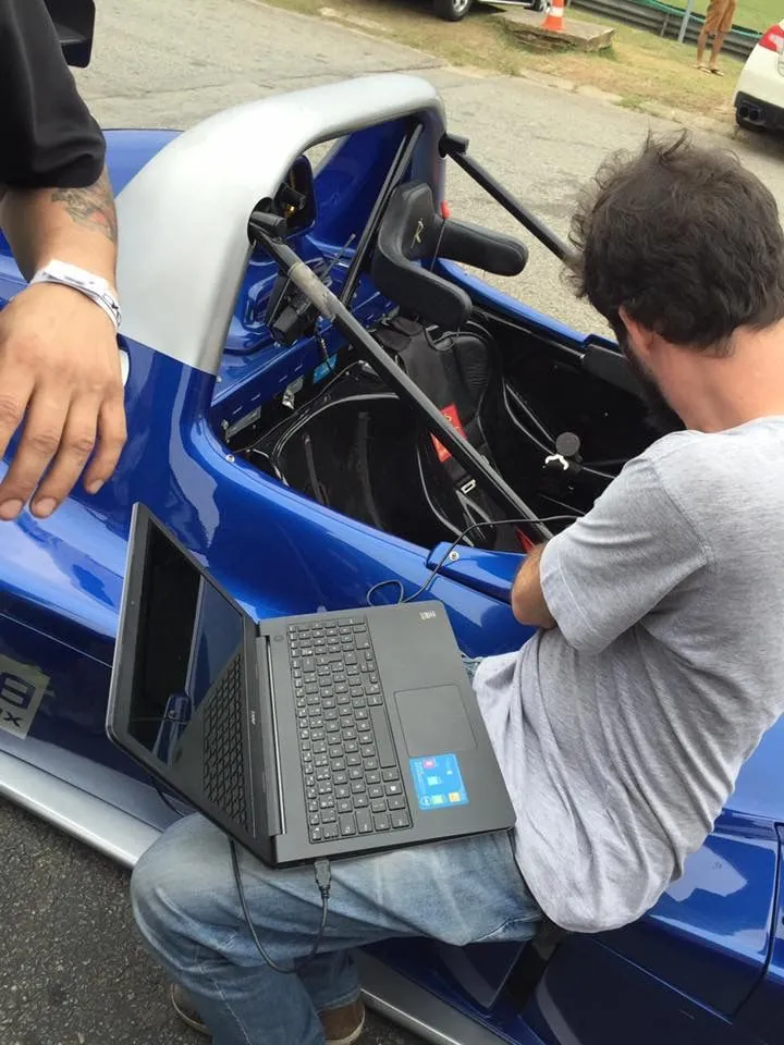Instrutor lendo os dados do carro no notebook, debruçado sobre o cockpit de um protótipo azul