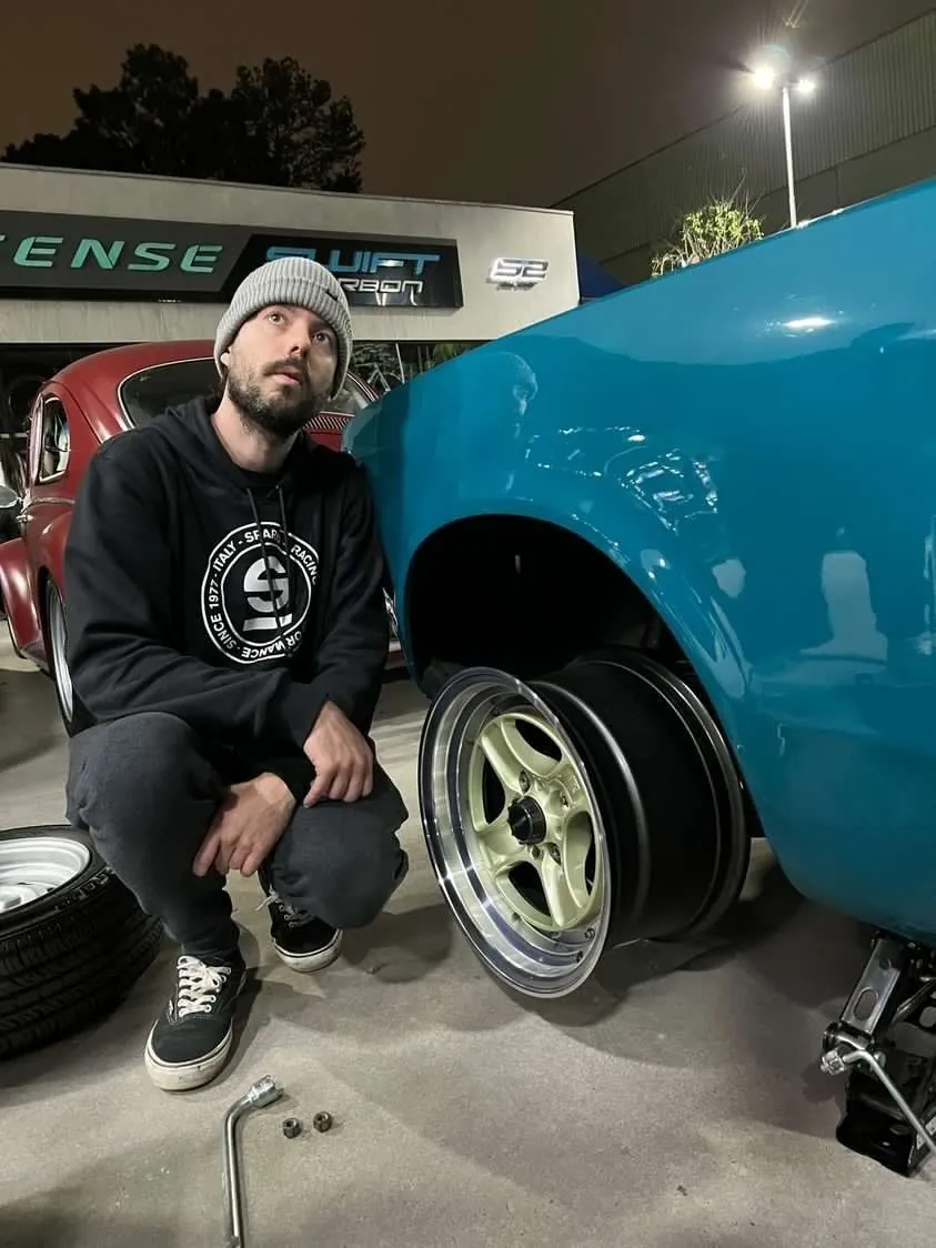 Ricardo agachado ao lado de um Chevette azul, conferindo o encaixe da roda Maui no paralama