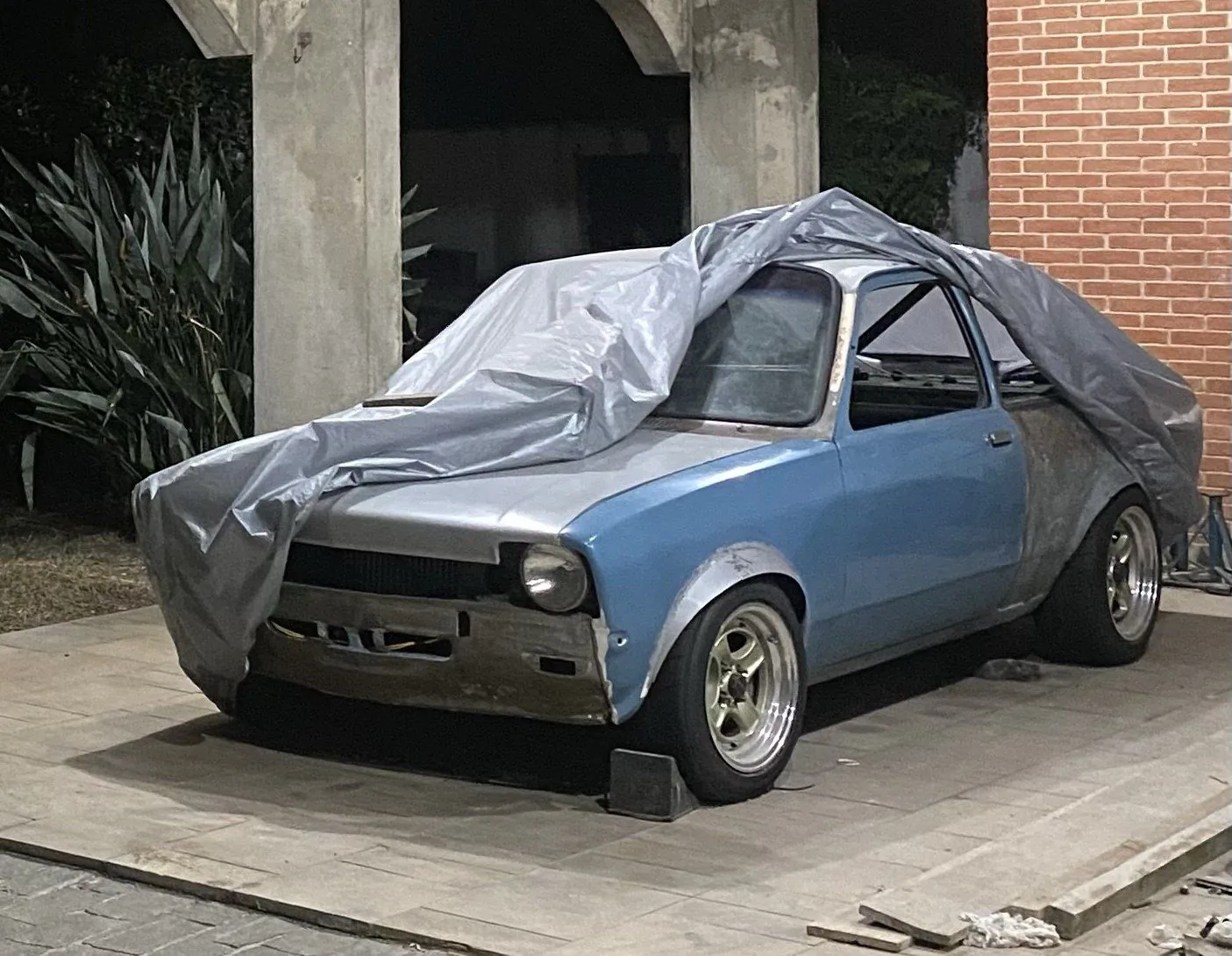 CHEV37TE parcialmente coberto por uma lona, à noite, estacionado na casa da avó de Ricardo