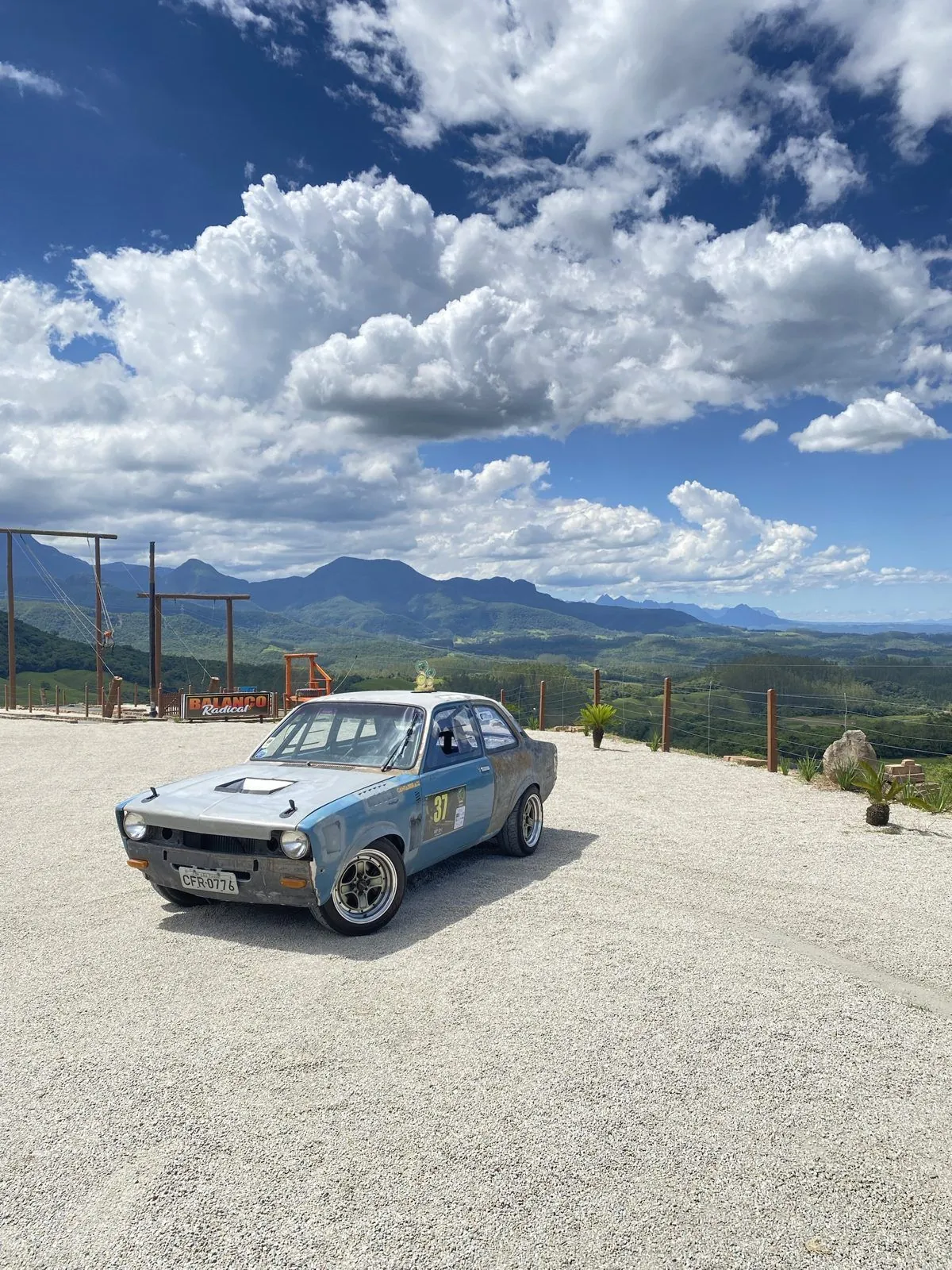 CHEV37TE com o número 37 na porta, estacionado num mirante com as montanhas da Serra do Rio do Rastro ao fundo