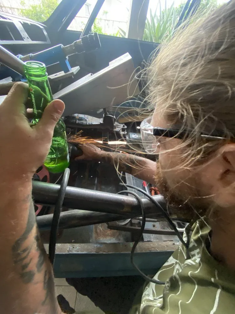Amigo cortando com esmerilhadeira dentro do carro, com uma cerveja na mão de quem fotografa
