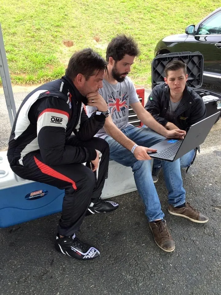 Ricardo, ao centro, analisando dados no notebook com o piloto de um Radical SR8 e outro integrante da equipe, nos boxes de Interlagos