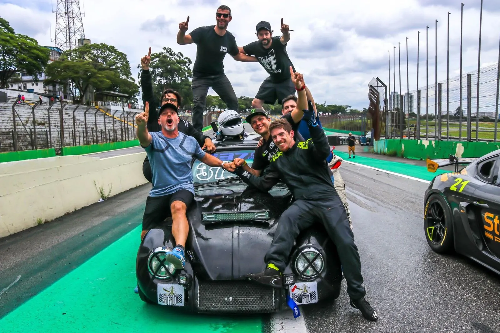 Equipe comemorando o título sobre o Fusca preto número 37 em Interlagos, com os dedos apontados para cima