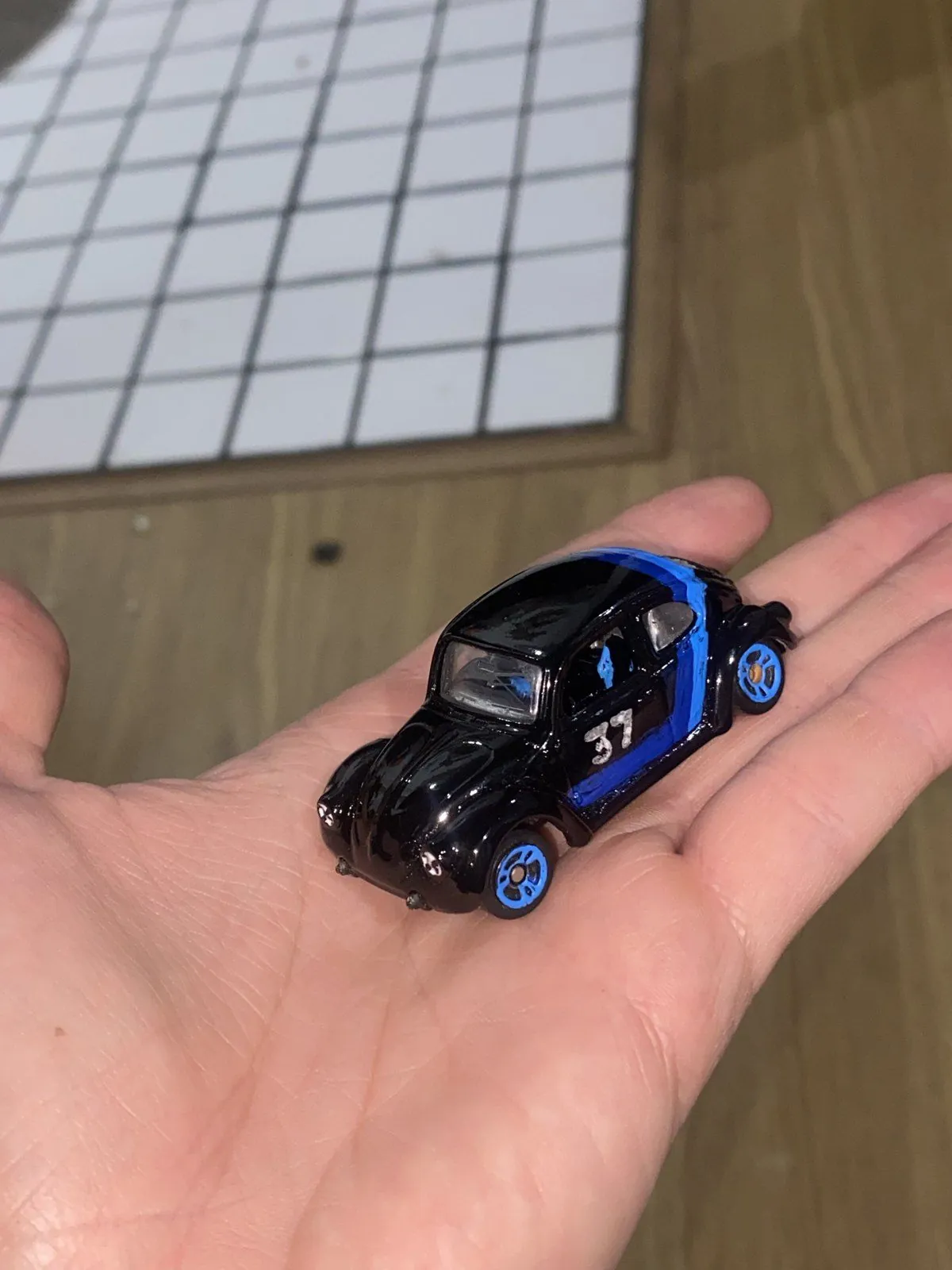 Miniatura do Fusca 37 na palma da mão, preta com faixas azuis e o número 37