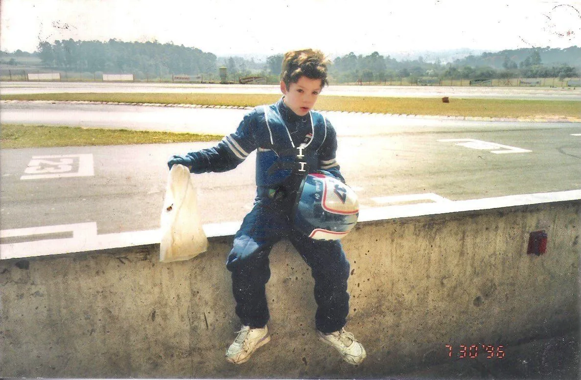 Ricardo criança de macacão, sentado no muro do kartódromo com o capacete no colo