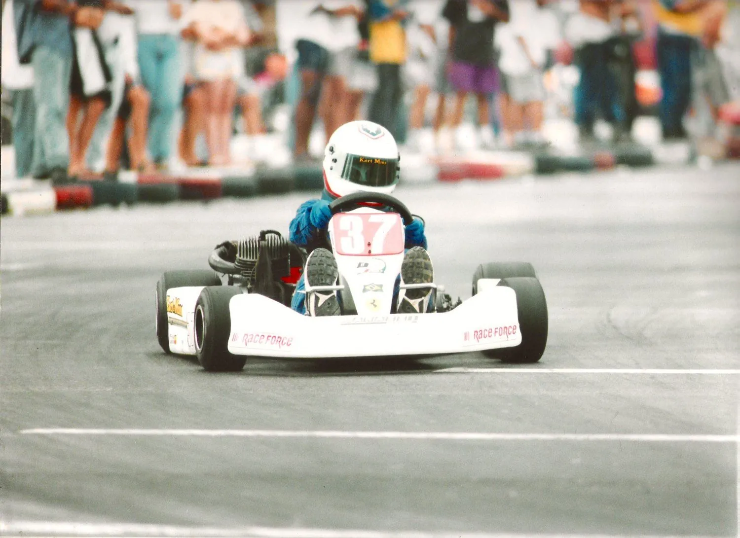 Ricardo criança pilotando o kart número 37, com o público atrás dos pneus de proteção