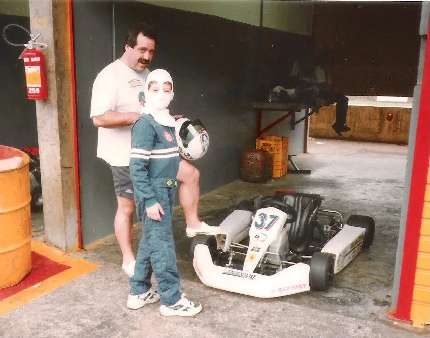 Ricardo criança de macacão e balaclava no box, ao lado do pai, Renato Rossini de Gouveia, e do kart número 37