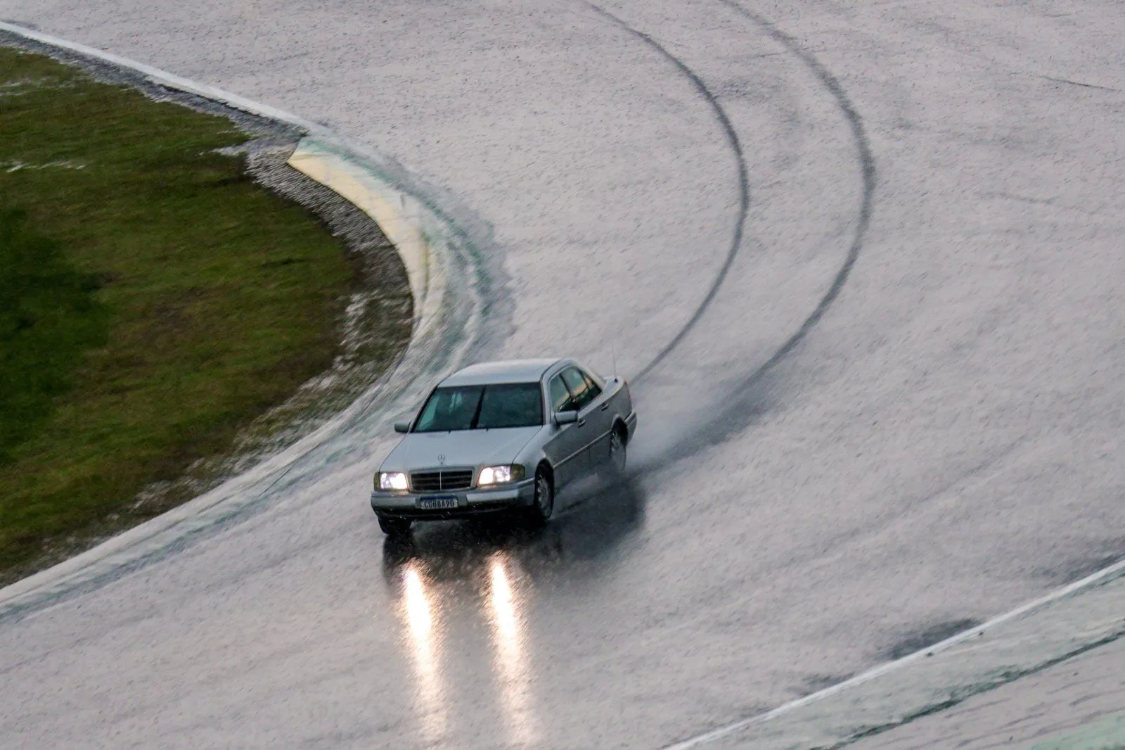 Mercedes C280 prata contornando curva de Interlagos com a pista molhada, faróis acesos