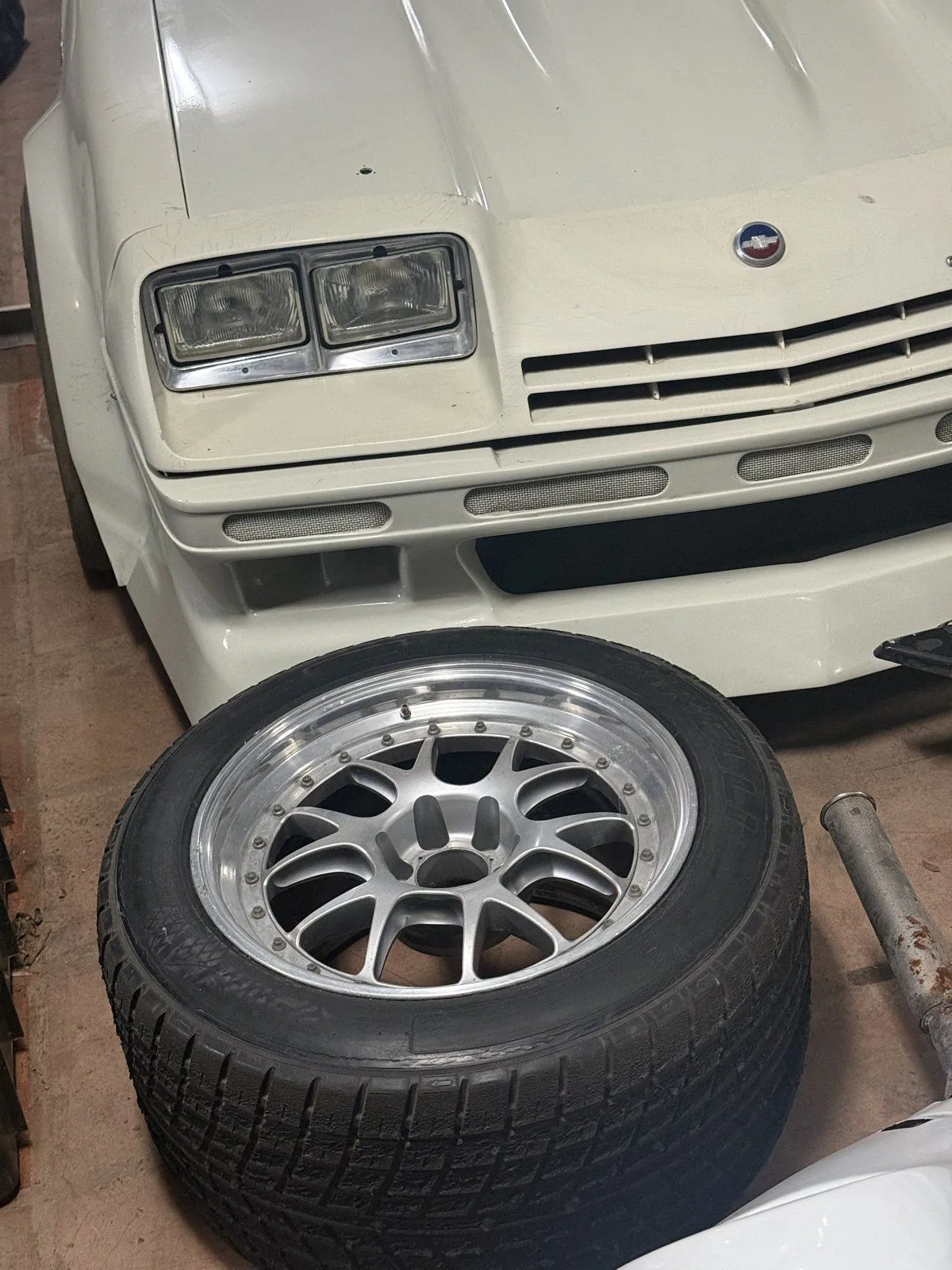 Roda BBS de três peças com pneu, apoiada em frente ao Monza 1975 branco