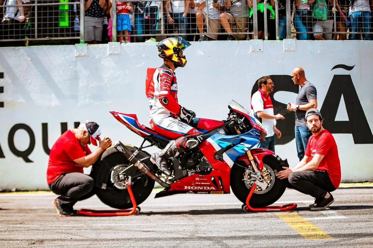 Ricardo agachado ao lado da roda dianteira de uma Honda de corrida da RP113 no grid