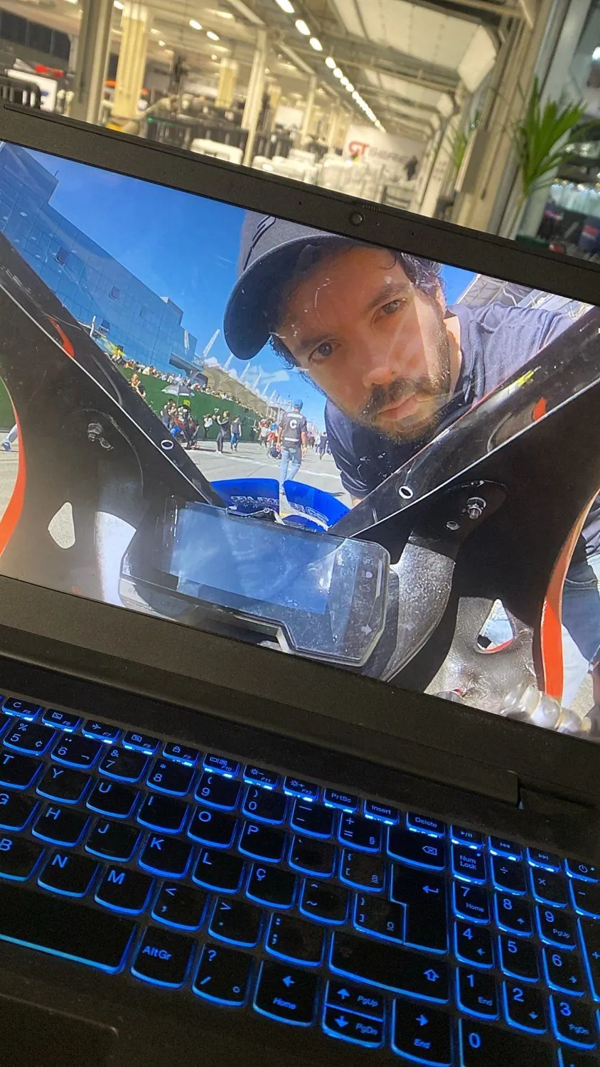 Tela do notebook mostrando a imagem da câmera onboard da moto, com Ricardo olhando para a lente